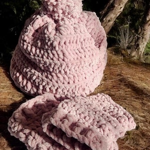 Könnte beinhalten: Eine rosa gestrickte Mütze mit einem Bommel oben und einem passenden Paar rosa gestrickter Fäustlinge.