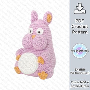 Puede incluir: Un juguete amigurumi de crochet rosa con forma de personaje Totoro de la película Mi vecino Totoro. El juguete tiene ojos grandes y redondos, una pequeña boca y una barriga blanca. El juguete está sentado sobre un fondo blanco.