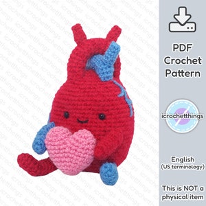 May include: A crochet pattern for a red heart-shaped anatomical heart holding a pink heart. The heart has a smiling face and blue crocheted details. The pattern is available as a PDF download. The text "This is NOT a physical item" is also included in the image.