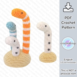 Op de afbeelding: Gehaakte wormspeelgoed in oranje, blauw en wit met zwarte stipdetails, staand op een bruine basis. De afbeelding bevat een PDF-haakpatroonafbeelding en de tekst "English (US terminology). This is NOT a physical item."