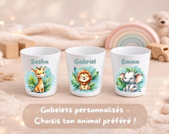 Può includere: Tre bicchieri di plastica bianchi con illustrazioni colorate di una giraffa, un leone e un elefante. Ogni bicchiere è personalizzato con i nomi Sasha, Gabriel ed Emma stampati in un carattere azzurro sopra le grafiche degli animali.