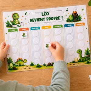 Peut inclure: Un tableau de propreté rectangulaire intitulé LÉO DEVIENT PROPRE ! illustré de dinosaures verts et d'un volcan, avec sept colonnes pour les jours de la semaine et des espaces circulaires blancs pour y apposer des petits autocollants carrés.