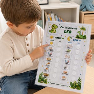 Puede incluir: Una tabla de rutina diaria plastificada titulada La routine de LEO con ilustraciones de dinosaurios, dividida en secciones de mañana y tarde con iconos de tareas y círculos vacíos, decorada con follaje verde y pequeñas estrellas amarillas.