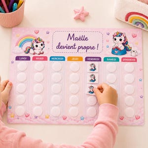 以下が含まれることがあります： ユニコーンのイラストと「Maëlle devient propre」というテキストが描かれた、長方形のピンク色のトイレトレーニング用ご褒美チャート。月曜日から日曜日までの各曜日の列があり、シールを貼るための円形のスペースが設けられています。