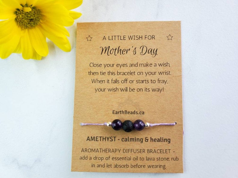 May include: A brown card with the text "A Little Wish For Mother's Day" and instructions for a wish bracelet. The bracelet is made with purple amethyst beads, black lava beads, and a silver bead. The bracelet is tied with a light purple string.