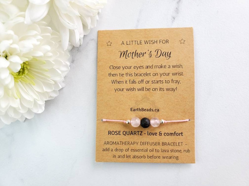 May include: A pink and silver bracelet with a lava stone bead and rose quartz beads. The bracelet comes with a card that says "A Little Wish for Mother's Day" and includes instructions for making a wish. The card also says "Rose Quartz - love & comfort" and "Aromatherapy Diffuser Bracelet - add a drop of essential oil to lava stone, rub in and let absorb before wearing."