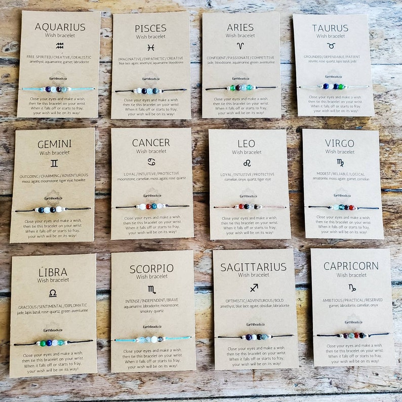 May include: Twelve cards with a brown background and white text. Each card features a zodiac sign symbol, name, and description. The cards are arranged in four rows of three. Each card has a wish bracelet with colourful beads and a string.