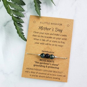 May include: A brown card with the text "A Little Wish For Mother's Day" and a green and black moss agate bracelet with a lava bead. The card says to close your eyes and make a wish, then tie the bracelet on your wrist. When it falls off or starts to fray, your wish will be on its way! EarthBeads.ca. The bracelet is described as a Moss Agate "the gardener's stone" grounding & protective aromatherapy diffuser bracelet. Add a drop of essential oil to lava stone, rub in and let absorb before wearing.