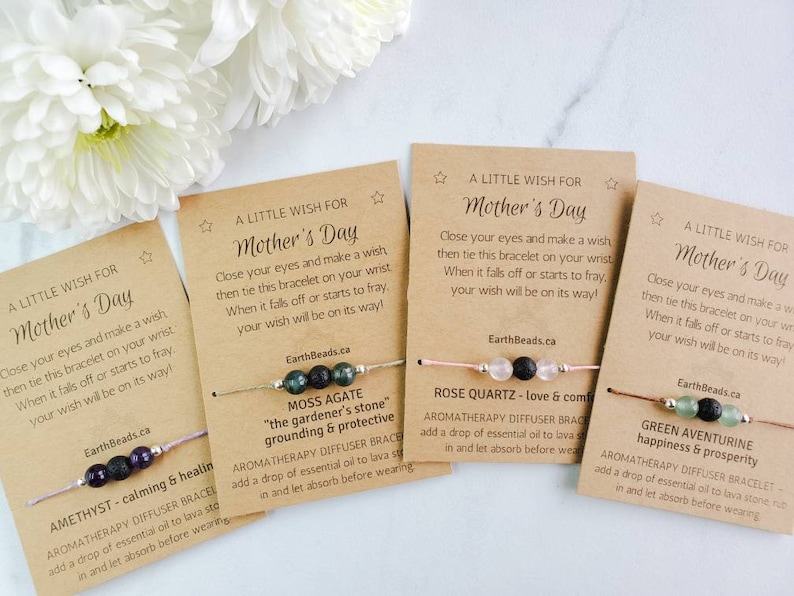 May include: Four Mother's Day bracelets with cards. Each bracelet has a different type of stone bead and a lava bead. The cards have a message about making a wish and tying the bracelet on your wrist. The stones are amethyst, moss agate, rose quartz, and green aventurine.