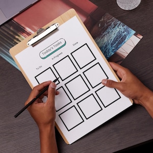 Puede incluir: Un portapapeles de madera con una lista de verificación impresa "Today's Tasks". La lista de verificación tiene secciones para "To Do", "In Progress" y "Done". Un bolígrafo negro se sostiene sobre la lista de verificación, listo para escribir. El portapapeles tiene un clip de metal plateado.
