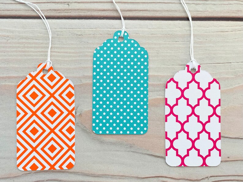 May include: Three gift tags with different geometric patterns. The first tag has a white and orange diamond pattern. The second tag has a white and teal polka dot pattern. The third tag has a white and pink quatrefoil pattern.