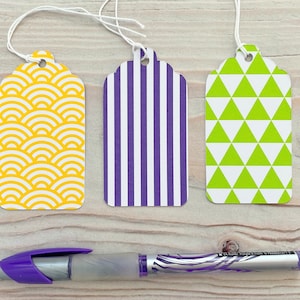 May include: Three gift tags with different patterns. The first tag has a yellow and white geometric pattern. The second tag has purple and white stripes. The third tag has green and white triangles.