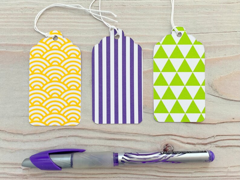 May include: Three gift tags with different patterns. The first tag has a yellow and white geometric pattern. The second tag has purple and white stripes. The third tag has green and white triangles.