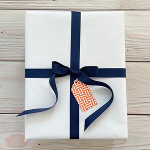 May include: A white gift box with a navy blue ribbon and bow. A small orange and white gift tag with a geometric pattern is attached to the ribbon.