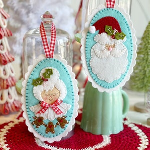 May include: Two felt Christmas decorations, one with a Santa Claus face and the other with a woman's face, both with red and white gingham ribbon.