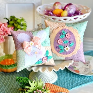 May include: Two handmade Easter pillows, one with a bunny design and the other with a floral design. Both pillows are made with patchwork fabric and feature embroidered details.