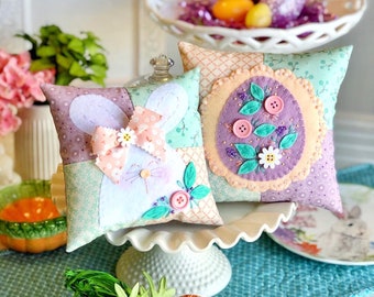 May include: Two handmade Easter pillows, one with a bunny design and the other with a floral design. Both pillows are made with patchwork fabric and feature embroidered details.