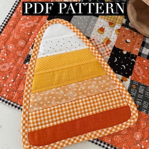 May include: A quilted fabric candy corn shape featuring horizontal stripes in white with black dots, yellow, light orange, and dark orange. The edges are finished with an orange and white gingham binding. The text PDF PATTERN is visible.