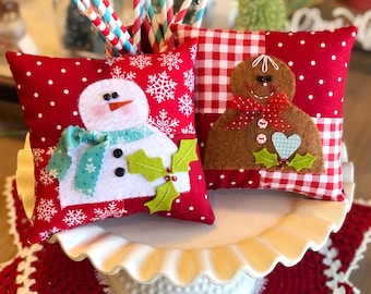 May include: Two handmade Christmas pillows, one with a snowman and the other with a gingerbread person. Both pillows are red and white with a patchwork design.