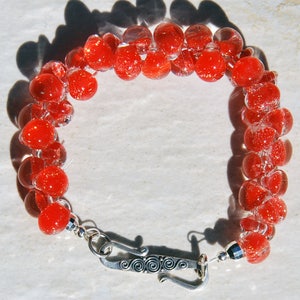 May include: A red glass bead bracelet with a silver clasp. The beads are clear with red flecks.