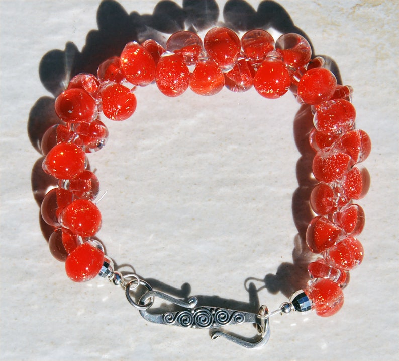 May include: A red glass bead bracelet with a silver clasp. The beads are clear with red flecks.