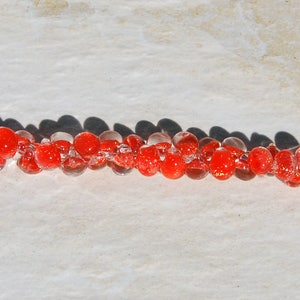 May include: A red glass bead bracelet with silver clasps. The beads are translucent and have a speckled appearance.