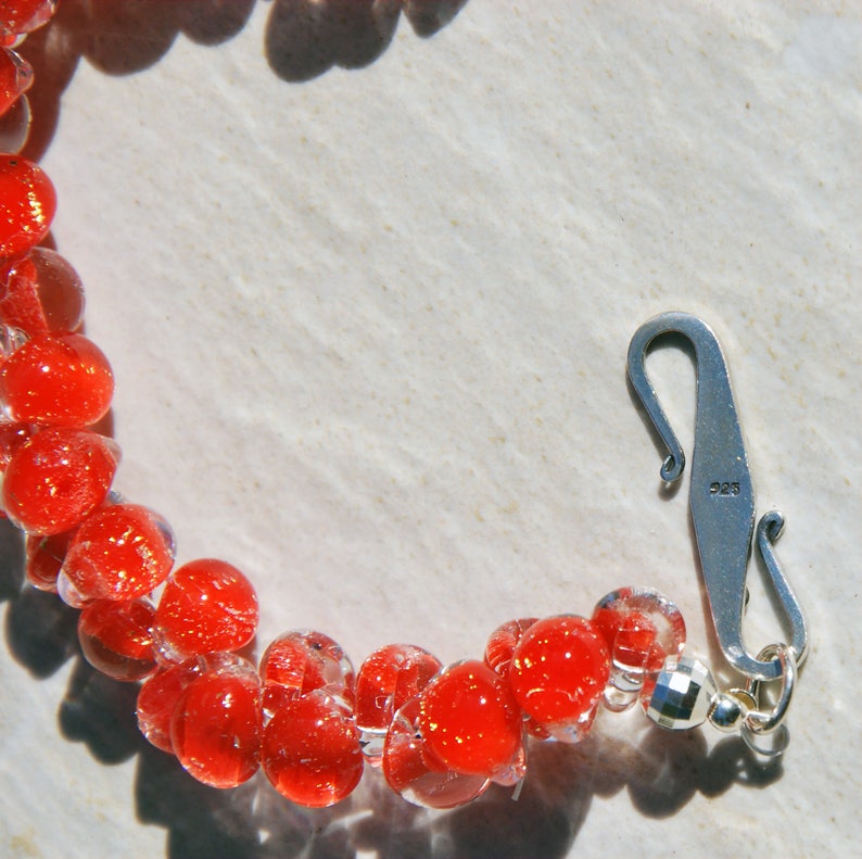 May include: A red glass bead necklace with a silver clasp. The clasp is marked with "925", indicating it is sterling silver.