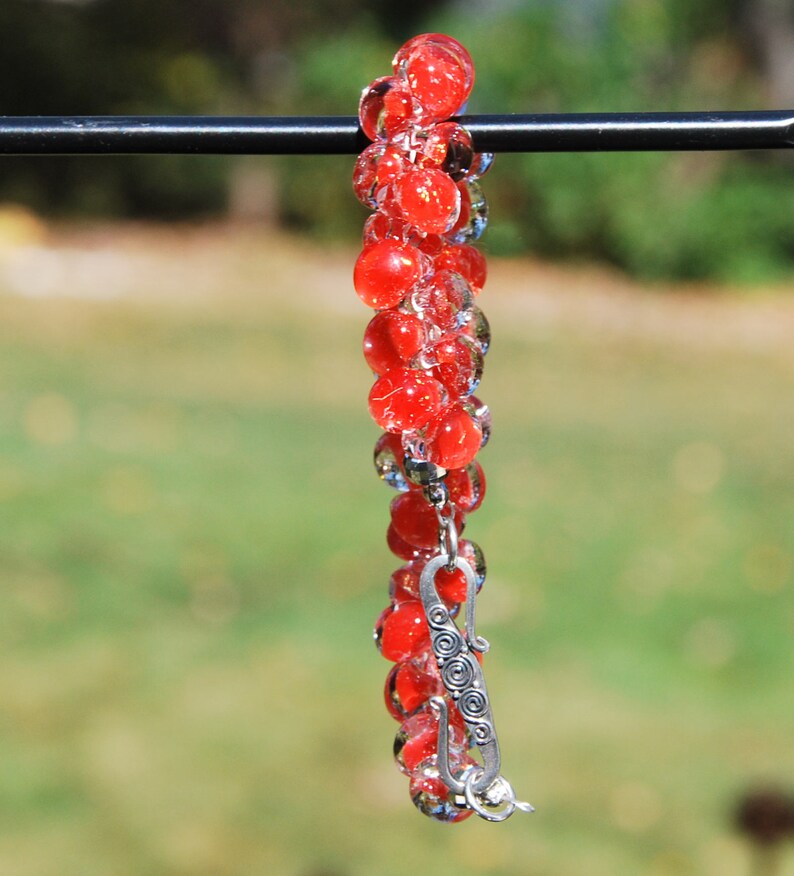May include: A red glass bead bracelet with a silver clasp. The beads are clear with a red tint and are strung together in a long strand.