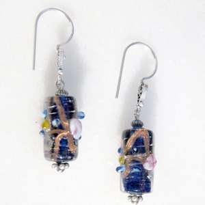 May include: A pair of dangle earrings featuring dark blue, cylindrical glass beads with copper-colored swirls and small, colorful accents. The earrings have silver-toned ear wires and decorative bead caps.
