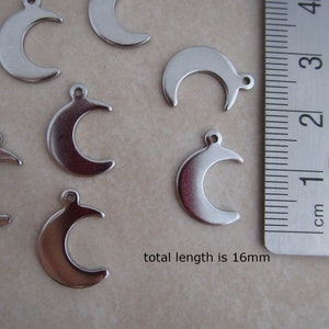 May include: A close-up of eight silver crescent moon charms, each measuring 16mm in length. The charms are arranged on a white surface next to a ruler.