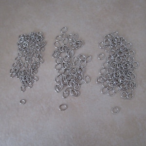 May include: Three piles of silver jump rings, a common jewelry making supply.