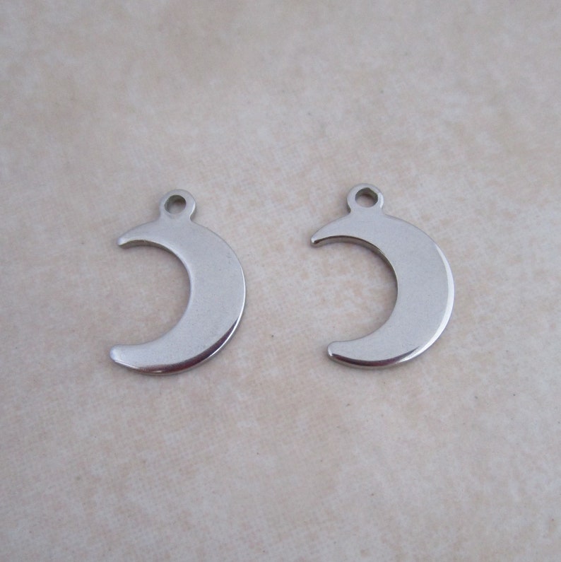 May include: Two silver crescent moon charms with a hole at the top for attaching to jewelry or other crafts.