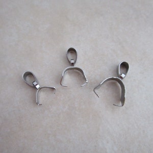 May include: Three silver-toned metal pendant bails, each with a loop at the top and a curved opening at the bottom. These bails are used for attaching pendants to necklaces or chains.