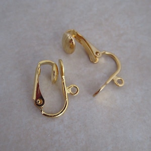 May include: Two gold-tone clip-on earring findings. Each finding has a small, round, flat pad on one end and a curved, open loop on the other end.