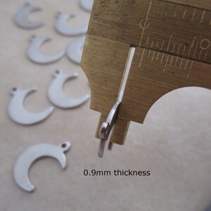 May include: Close-up of a silver crescent moon charm measured with calipers. The charm is 0.9mm thick.