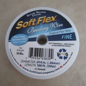 May include: A spool of Soft Flex Beading Wire in satin silver color. The wire is fine, knot tying, stainless steel, and nylon coated. It has a test strength of 10 lbs. The spool is labeled with the brand name, product details, and a barcode. The spool is made in the USA.