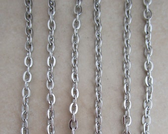 May include: Five strands of silver chain, each with a different length, hanging against a light beige background.