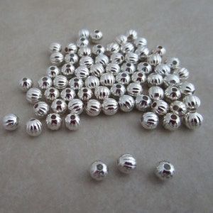 May include: A large pile of silver-colored round beads with a ridged texture. The beads are arranged in a random pattern.