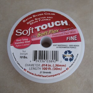 May include: A spool of silver colored Soft Touch Soft Flex Premium Flex Wire, labeled "Fine" and "Soft Materials - Seed Beads & Freshwater Pearls". The spool is 100 feet long and 0.014 inches in diameter. The label also states "Knot Tying Stainless Steel Nylon Coated" and "Test Strength 10 lbs.".