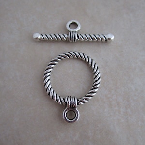 May include: Silver tone twisted rope toggle clasp with a ring and a bar. The clasp is designed for necklaces, bracelets, or other jewelry projects.