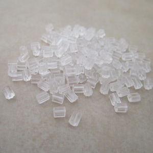 May include: A pile of clear, cylindrical earring backs. These small, transparent earring stoppers are made of a soft, flexible material. The earring backs are designed to secure earrings in place and prevent them from falling out.