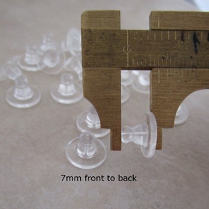 May include: Close-up of a caliper measuring the height of a clear plastic earring back. The caliper reads 7mm front to back.