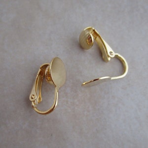 May include: A pair of gold-tone clip-on earring findings with round, flat pads. The pads are smooth and have a shiny finish.
