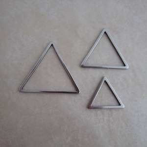 May include: Three silver triangle-shaped metal charms. The charms are different sizes, with the largest charm being at the top of the image and the smallest charm at the bottom.