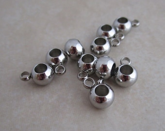 May include: A group of silver metal bead caps with a hole in the center and a loop on each side. The bead caps are arranged in a random pattern on a light gray surface.