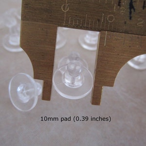 May include: Close-up of a clear plastic earring back with a 10mm pad, measured with a ruler. The text "10mm pad (0.39 inches)" is visible below the ruler.