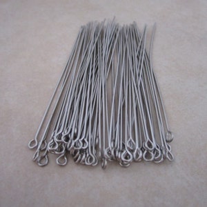 May include: A pile of silver-toned head pins with eye loops. The head pins are arranged in a fan shape.