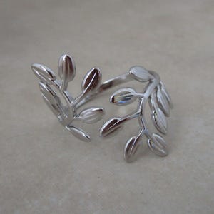 May include: A silver-colored ring featuring a botanical design. The ring wraps around the finger and is adorned with detailed leaf-shaped elements. The leaves are arranged in a symmetrical pattern, creating an elegant and nature-inspired accessory.