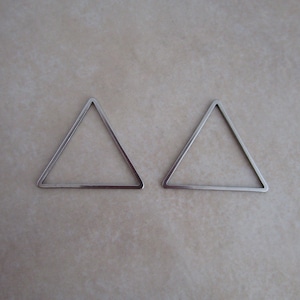 May include: Two silver triangle-shaped metal hoops. The hoops are open and have a smooth, polished finish.