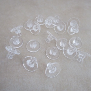 May include: A close-up of a group of clear plastic earring backs. The backs are designed to be used with post earrings.
